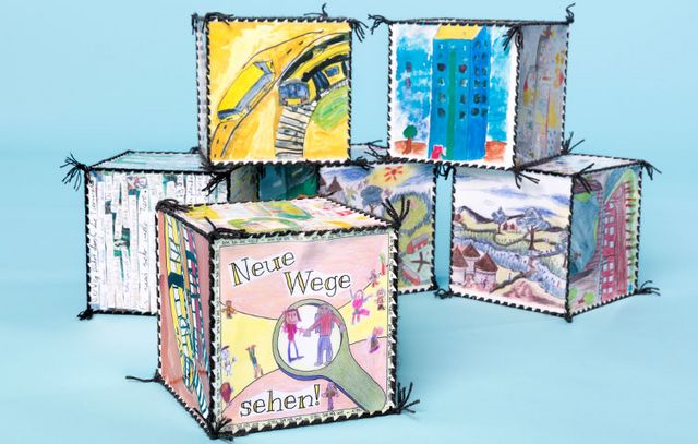 Auf dem Bild sind sechs selbstgebastelte Würfel mit unterschiedlichen Motiven abgebildet. Im Vordergrund ist auf einem der Würfel der Schriftzug „Neue Wege sehen“ abgebildet. 